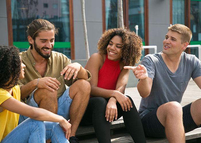 A group of friends smiling and talking outdoors, demonstrating psychological tricks people use on themselves and others.