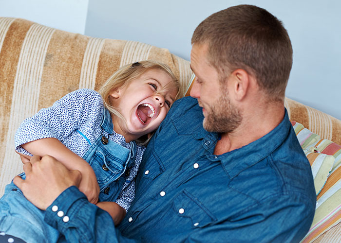 Man and child sharing a joyful moment on a couch, illustrating psychological tricks people use on themselves and others.
