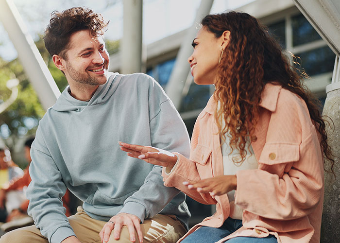 Two people smiling and using psychological tricks to connect in an outdoor social setting with natural light.