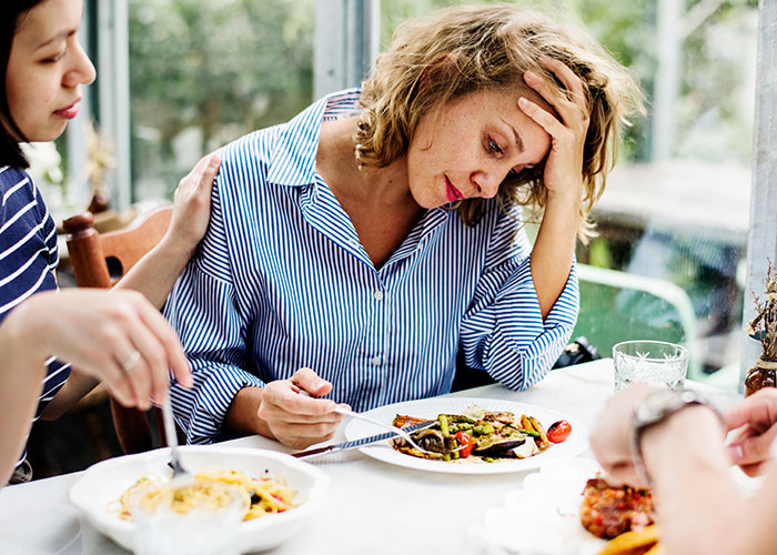 Woman showing signs of distress while eating, comforted by another person using psychological tricks that influence behavior.