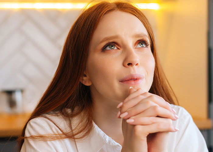 Young woman with red hair thoughtfully gazing upward, illustrating psychological tricks people use on themselves and others.