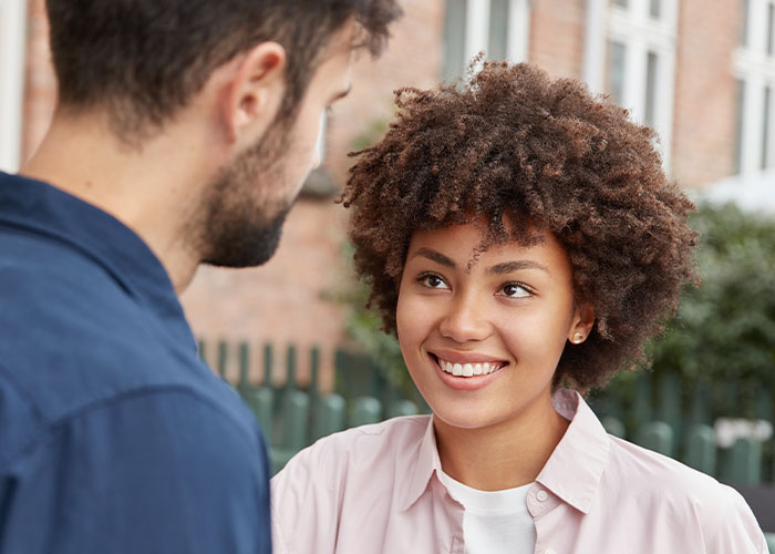 Young woman smiling while talking to a man outdoors, illustrating psychological tricks people use on themselves and others.