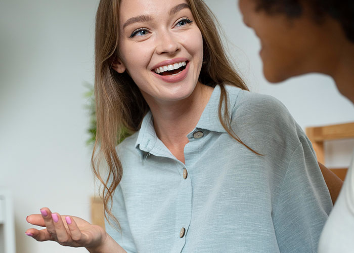 Young woman smiling and using psychological tricks in a friendly conversation with another person indoors.
