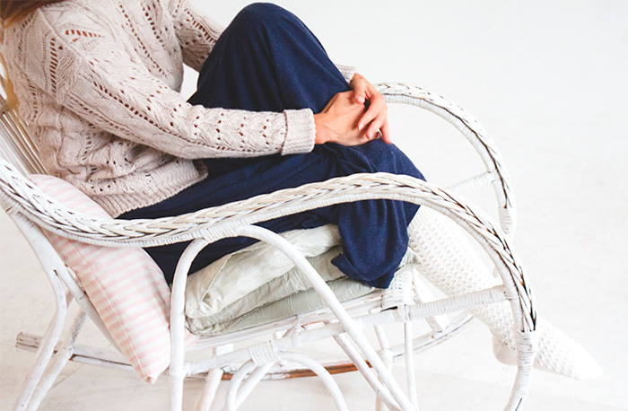 Person sitting crossed-legged in white wicker chair wearing cozy knit sweater and leggings, suggesting hidden test by therapist.