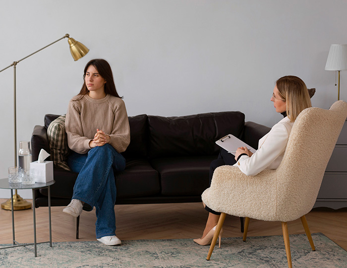 Woman in casual clothes sitting on sofa during therapy session as therapist observes using hidden test to judge.