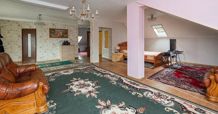 Spacious real estate listing with vintage leather furniture, floral wallpaper, and multiple colorful oriental rugs in an open living area.