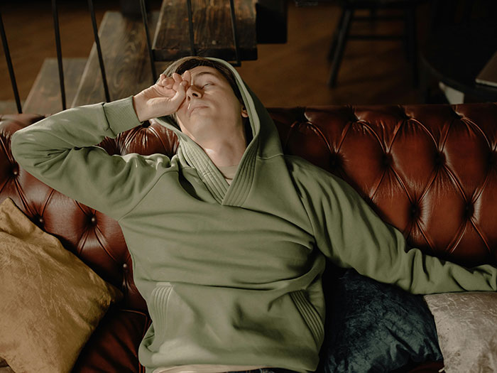 Tired parent in green hoodie sitting on a leather couch, showing signs of unhappiness and exhaustion at home.