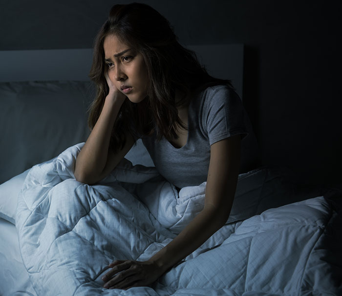 Woman awake in bed at night, troubled by roommate’s snoring, unable to sleep under dim bedroom lighting.