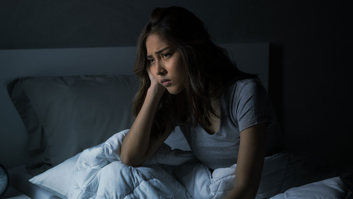 Woman sitting awake in bed at night, frustrated and tired due to roommateu2019s snoring keeping her awake.