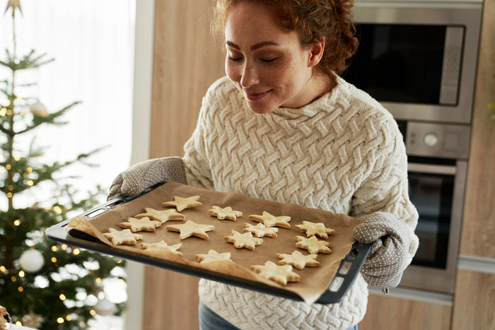 A woman holding a baking tray with freshly baked cookies, smiling proudly after perfecting secret cookie recipe.