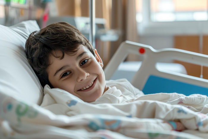 Smiling boy lying in hospital bed, appearing nonverbal and bedridden, in a medical care setting. Smiling boy lying in hospital bed, appearing nonverbal and bedridden, in a medical care setting.