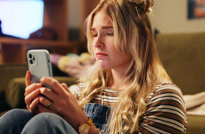 Teen sitter looking concerned at phone while seated indoors, reflecting on caring for a nonverbal bedridden boy. Teen sitter looking concerned at phone while seated indoors, reflecting on caring for a nonverbal bedridden boy.