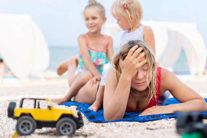 Frustrated woman overwhelmed by kids on beach, illustrating conflict with babysitting on vacation and personal time. Frustrated woman overwhelmed by kids on beach, illustrating conflict with babysitting on vacation and personal time.