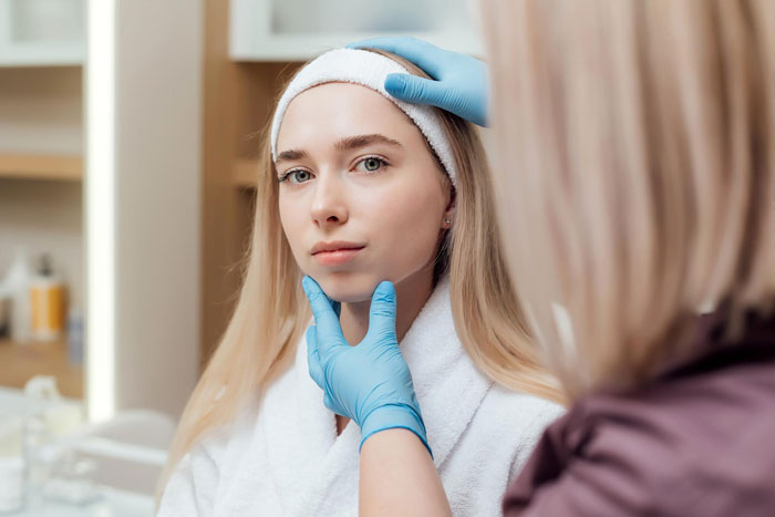 Young woman getting a facial consultation in a spa setting, considering options for a BBL cosmetic procedure.