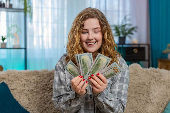 Young woman smiling at cash in hand, representing 18YO planning to spend grandpa's inheritance on a BBL. Young woman smiling at cash in hand, representing 18YO planning to spend grandpa's inheritance on a BBL.