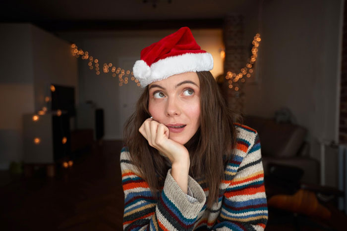 Young woman wearing a Santa hat and striped sweater, looking thoughtful amid festive Christmas lights indoors during the holiday season. Young woman wearing a Santa hat and striped sweater, looking thoughtful amid festive Christmas lights indoors during the holiday season.