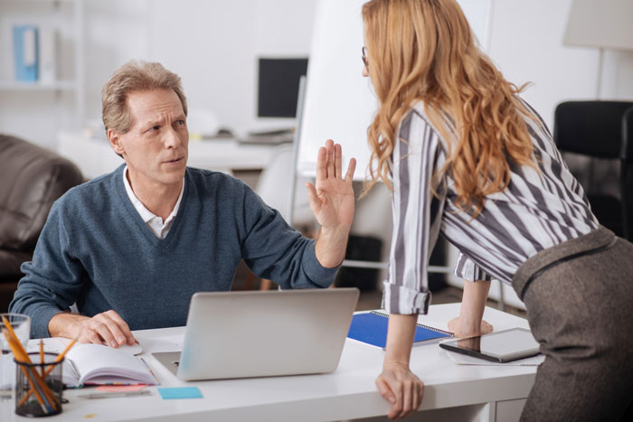 Man refusing to train replacement without pay, raising hand in disagreement during office conversation with woman. Man refusing to train replacement without pay, raising hand in disagreement during office conversation with woman.