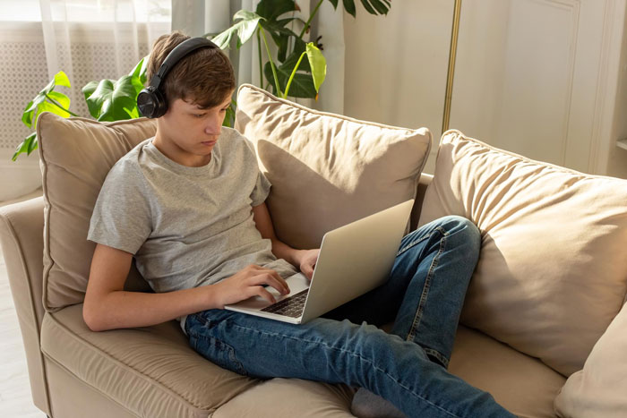 Teen boy with headphones using laptop on couch, representing abandoned son reconnecting with siblings in a happy family setting. Teen boy with headphones using laptop on couch, representing abandoned son reconnecting with siblings in a happy family setting.