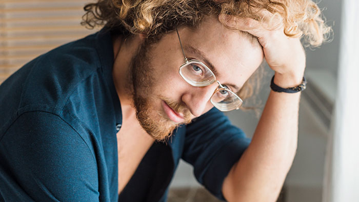 Young man with glasses looking stressed and contemplative, illustrating people's lies getting out of hand and impacting lives.