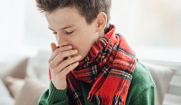 Young boy in green sweater and red scarf covering mouth, illustrating the consequences of people's lies getting out of hand.