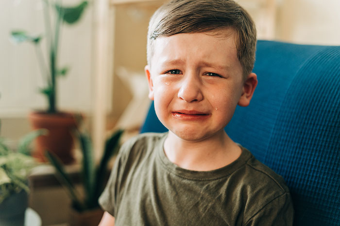 Boy with tear-streaked face sitting on a blue couch, showing emotion related to people's lies getting out of hand.