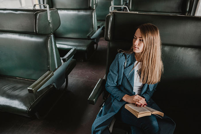 Young woman sitting alone on a bus, holding a book, reflecting on how people's lies got way out of hand.