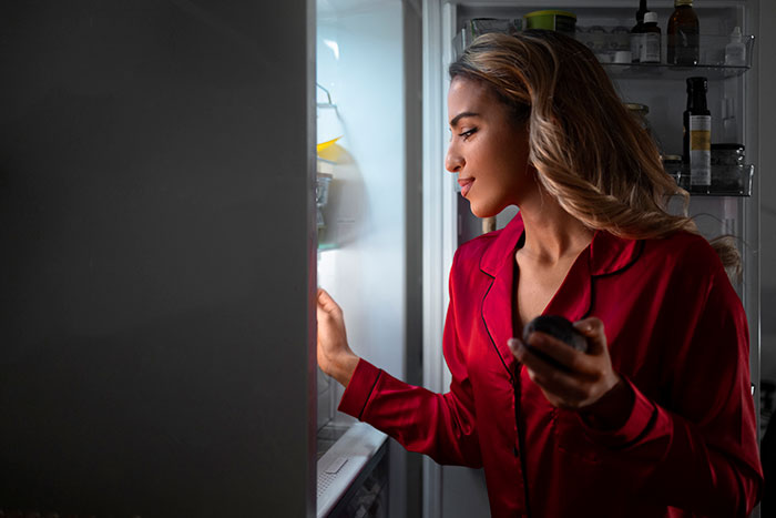 Woman in red pajamas looking inside a fridge at night, illustrating moments when people’s lies got out of hand.