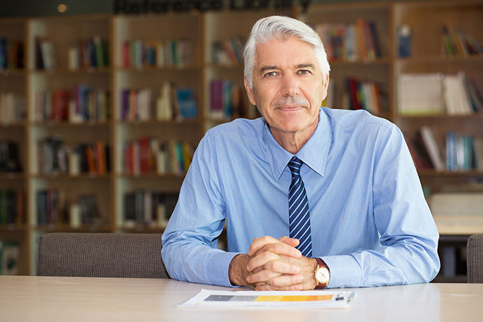 Mature man in a blue shirt sitting at a table, representing stories where people's lies got out of hand and changed lives.