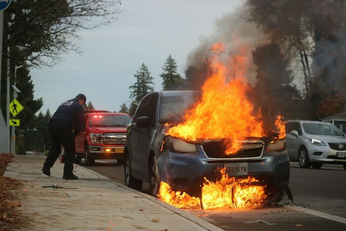 Car engulfed in flames on street, emergency responders at the scene during bizarre moments causing shock and disbelief.