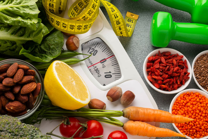 Healthy foods and measuring tape surrounding a weight scale, illustrating strict diet and health nut concepts. Healthy foods and measuring tape surrounding a weight scale, illustrating strict diet and health nut concepts.