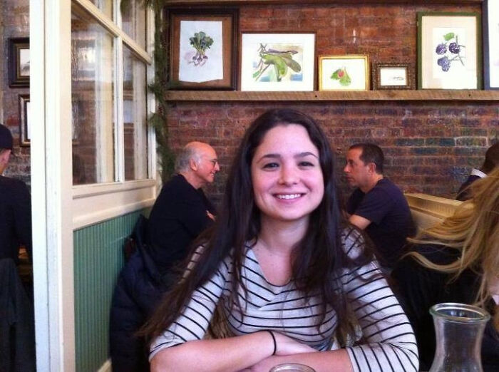 Young woman smiling at a cafe table with men in the background creating an epic photobomb that stole the show.