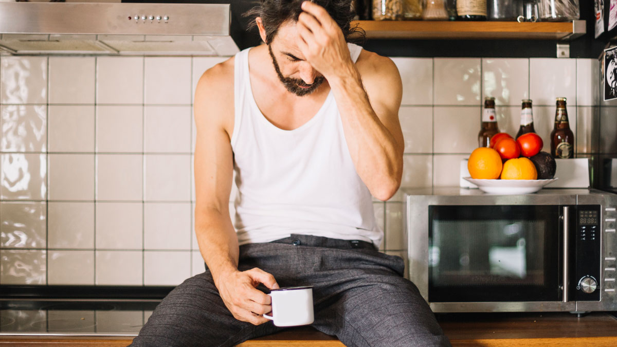 Grieving dad sitting in kitchen holding mug, looking down, trying to make daughter's birthday special despite challenges.