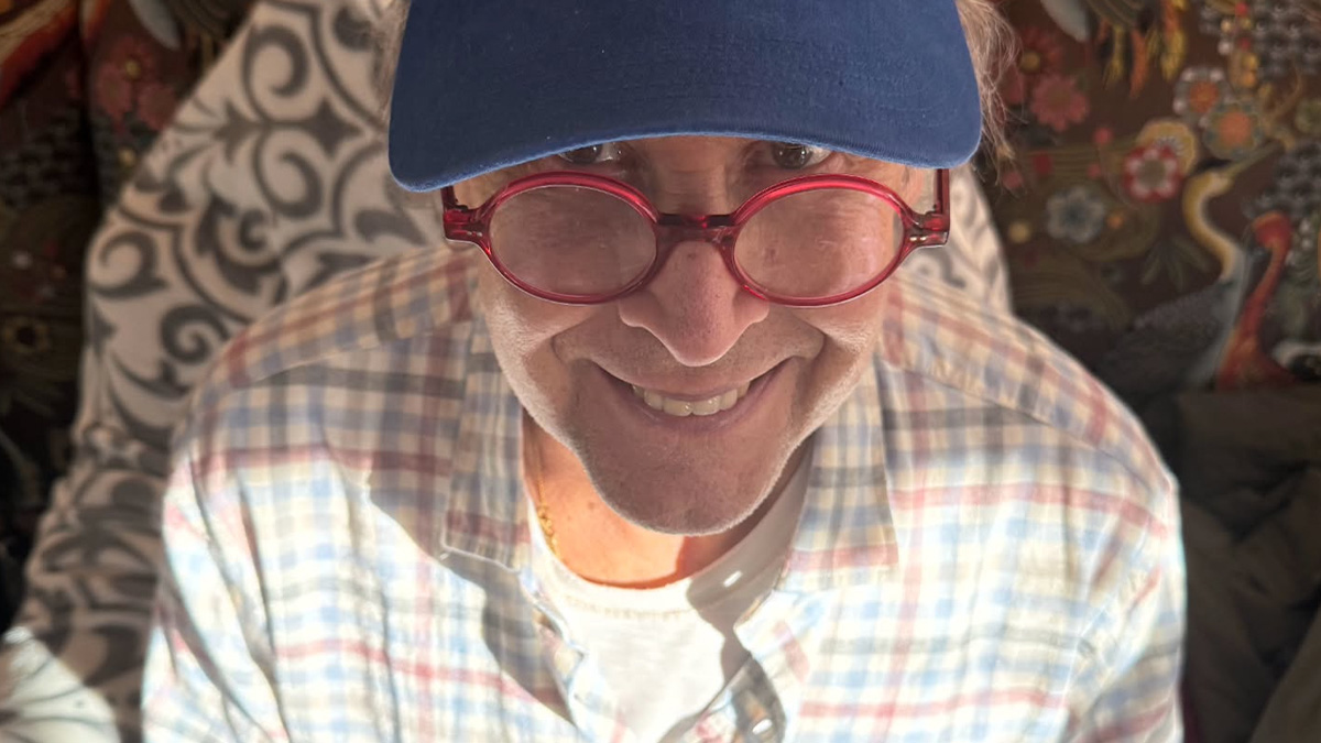 Man in red glasses and blue cap smiling indoors with patterned cushions, illustrating people no longer respect or like these celebrities.