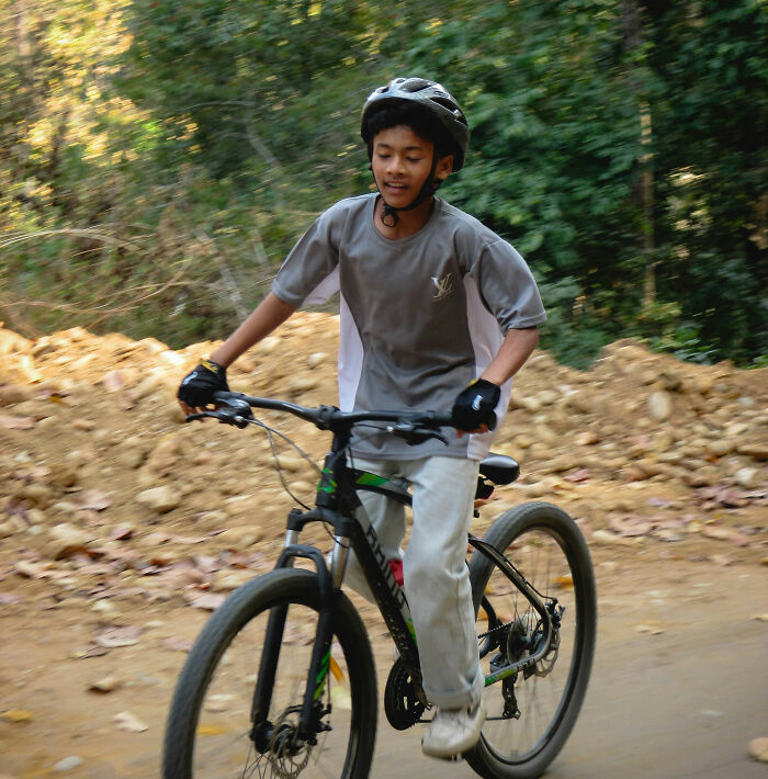 Boy wearing helmet riding a mountain bike on dirt path surrounded by trees, capturing real-life horror story moment outdoors.