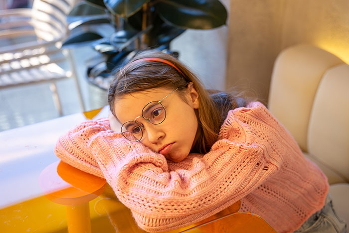 Sad young girl in pink sweater resting head on folded arms, feeling ignored and hurt due to family work priorities. Sad young girl in pink sweater resting head on folded arms, feeling ignored and hurt due to family work priorities.