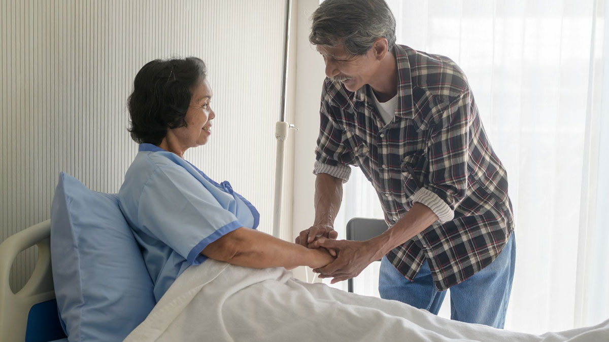 Man holding hands with woman in hospital bed, sharing a heavy confession and emotional moment together.