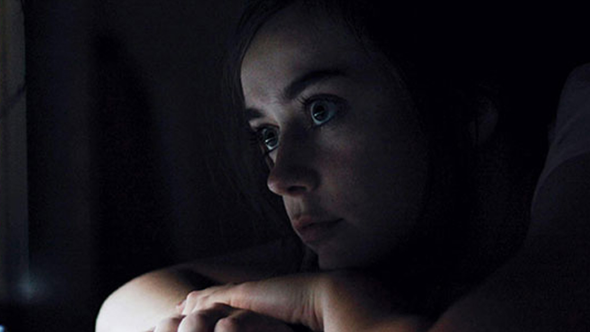 Young woman in dark room with a worried expression, portraying fear from the most terrifying things found online.