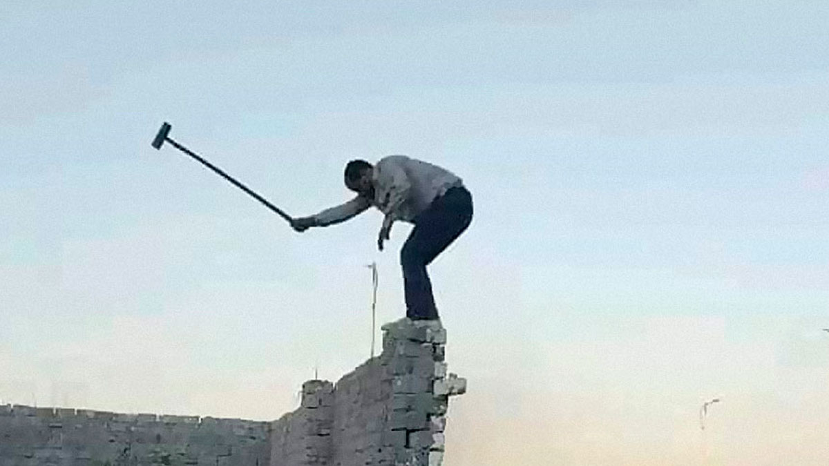 Man frozen in midair on crumbling brick wall holding a hammer in a dramatic frozen frame moment outside.