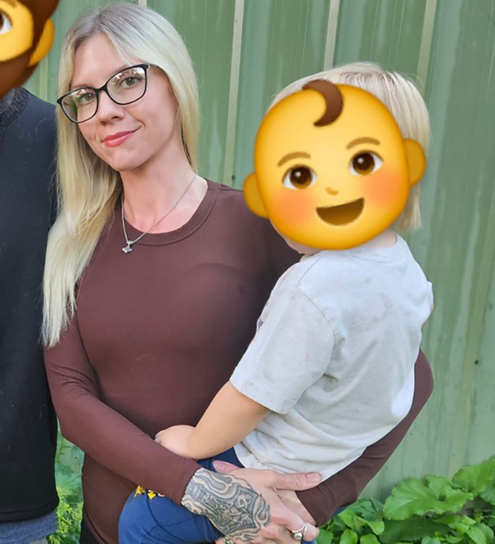 Woman with tattooed hand holding young child with covered face outdoors, related to viral autistic boy playground clash trial Woman with tattooed hand holding young child with covered face outdoors, related to viral autistic boy playground clash trial