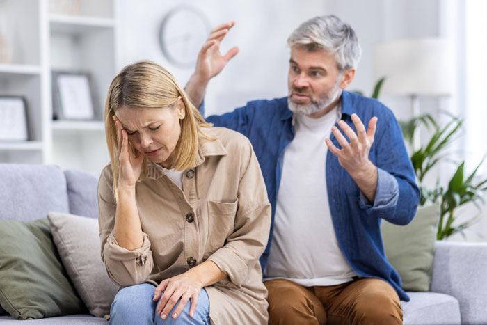 Woman called poor by stepdad arguing with him while she looks distressed on a couch in a home setting Woman called poor by stepdad arguing with him while she looks distressed on a couch in a home setting