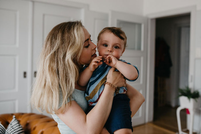 Woman feeling sick at home holding baby, appearing to ask husband for money in a cozy living room setting Woman feeling sick at home holding baby, appearing to ask husband for money in a cozy living room setting