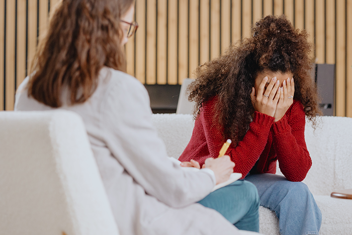 Woman with curly hair distressed and covering face during counseling session about cheating while wife is pregnant and postpartum. Woman with curly hair distressed and covering face during counseling session about cheating while wife is pregnant and postpartum.