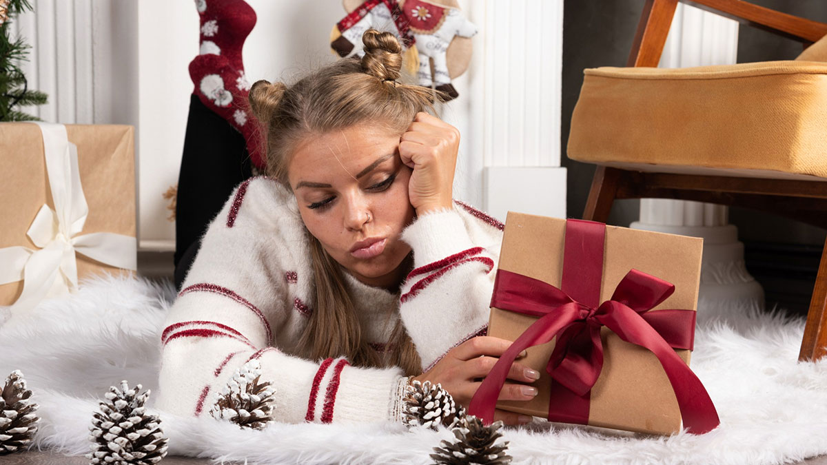 Young woman lying on floor looking sad next to wrapped gift, illustrating signs child never loved properly emotions.