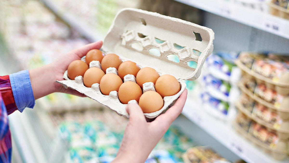 Person holding a carton of brown eggs while shopping in a grocery store, illustrating college experience habits in America