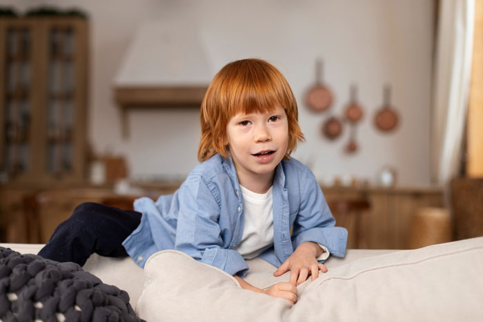 Young boy with red hair lying on a couch, illustrating a badly behaved nephew in a family babysitting conflict. Young boy with red hair lying on a couch, illustrating a badly behaved nephew in a family babysitting conflict.