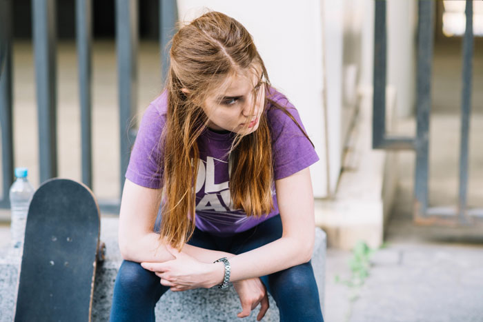 Teen girl feeling trapped and isolated, sitting near skateboard, struggling with mentally unstable sister and family dynamics.