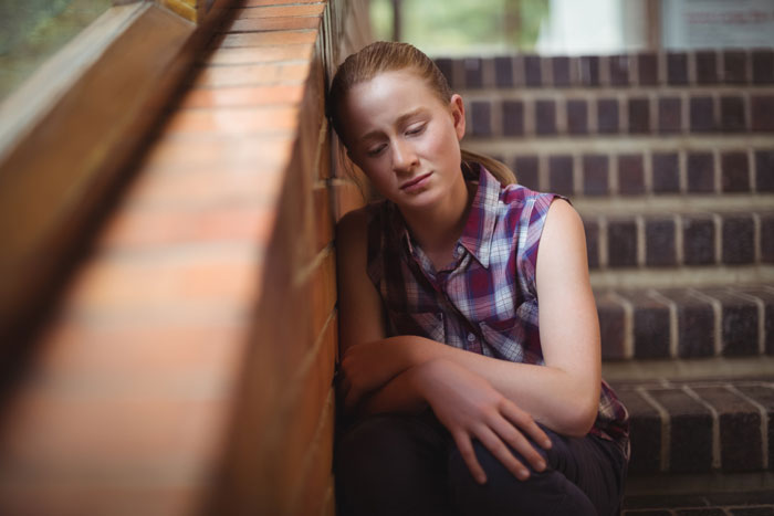 Teen girl sitting on stairs looking distressed feeling like a prisoner around mentally unstable sister and ignored by parents