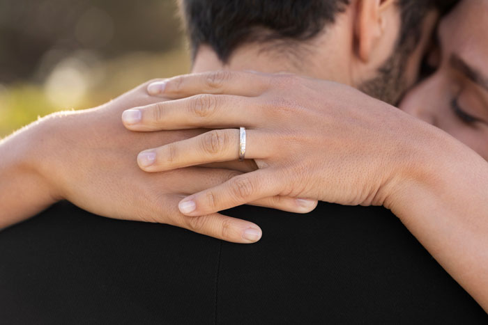Close-up of a couple embracing, highlighting a wedding ring symbolizing a big wedding and family tensions. Close-up of a couple embracing, highlighting a wedding ring symbolizing a big wedding and family tensions.