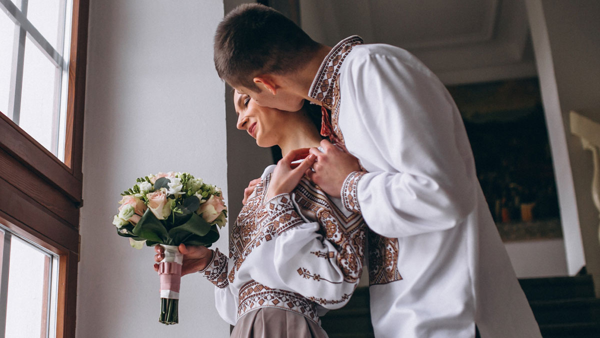 Couple in traditional attire near window, bride holding bouquet, highlighting big wedding and rejection sensitive dysphoria theme.
