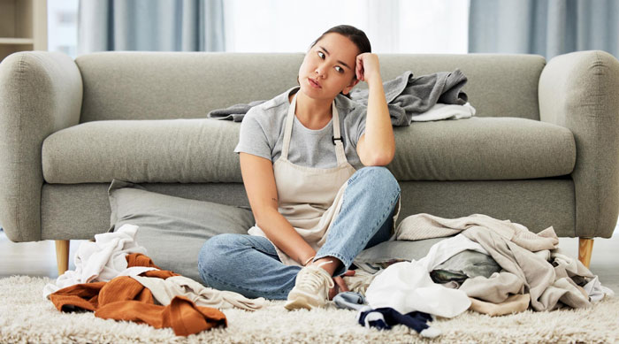 Woman sitting on floor surrounded by laundry, looking frustrated about cleaning and pest issues after sister moved in. Woman sitting on floor surrounded by laundry, looking frustrated about cleaning and pest issues after sister moved in.